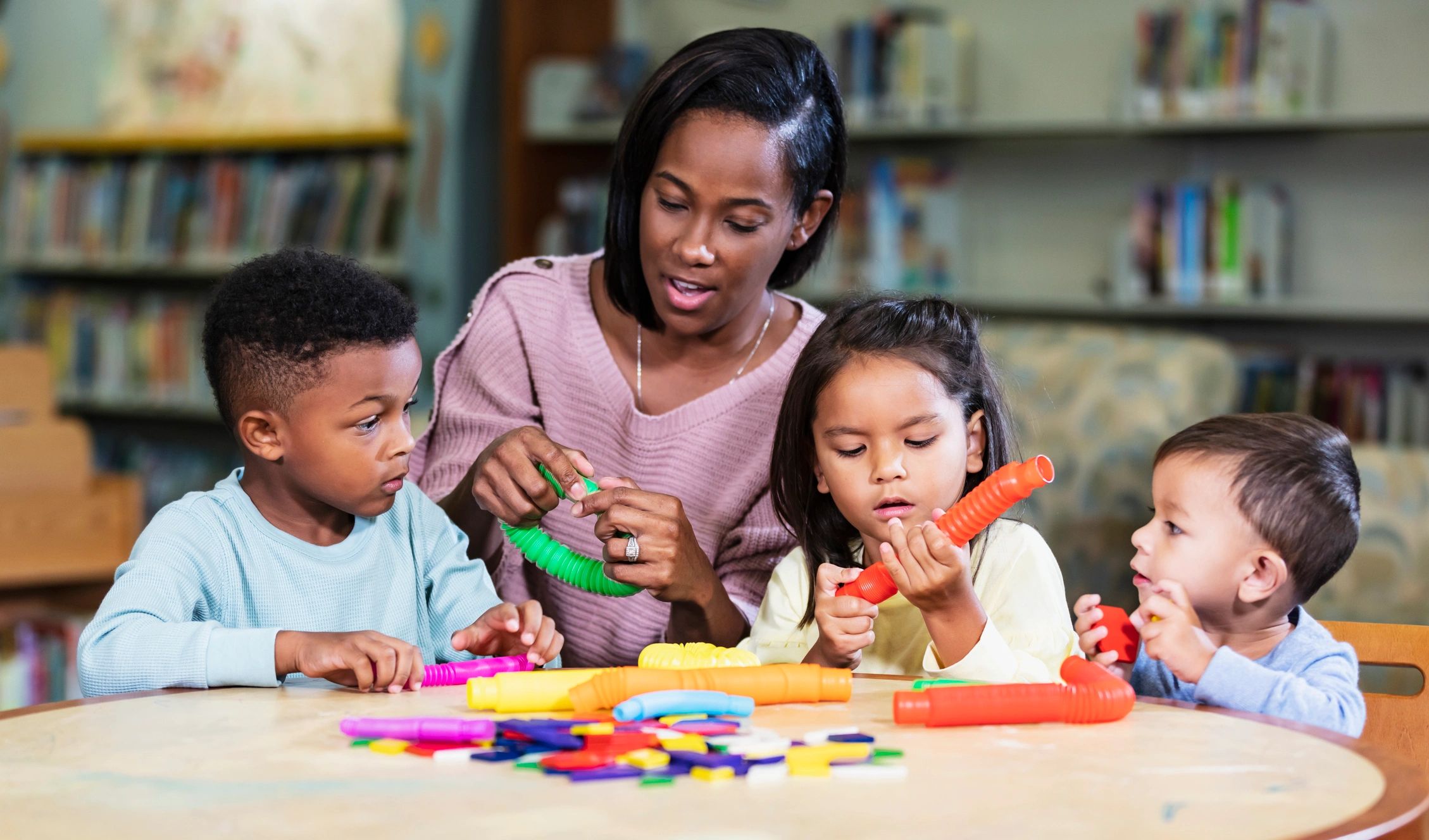 Teacher and preschool children playing with colorful toys at a table