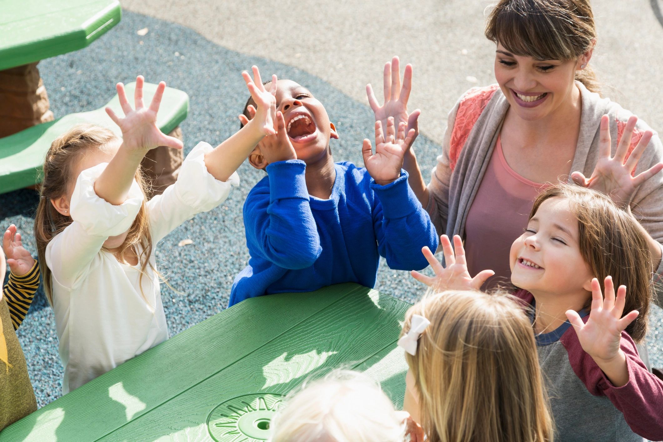 Preschool teacher and children laughing at an outdoor activity table